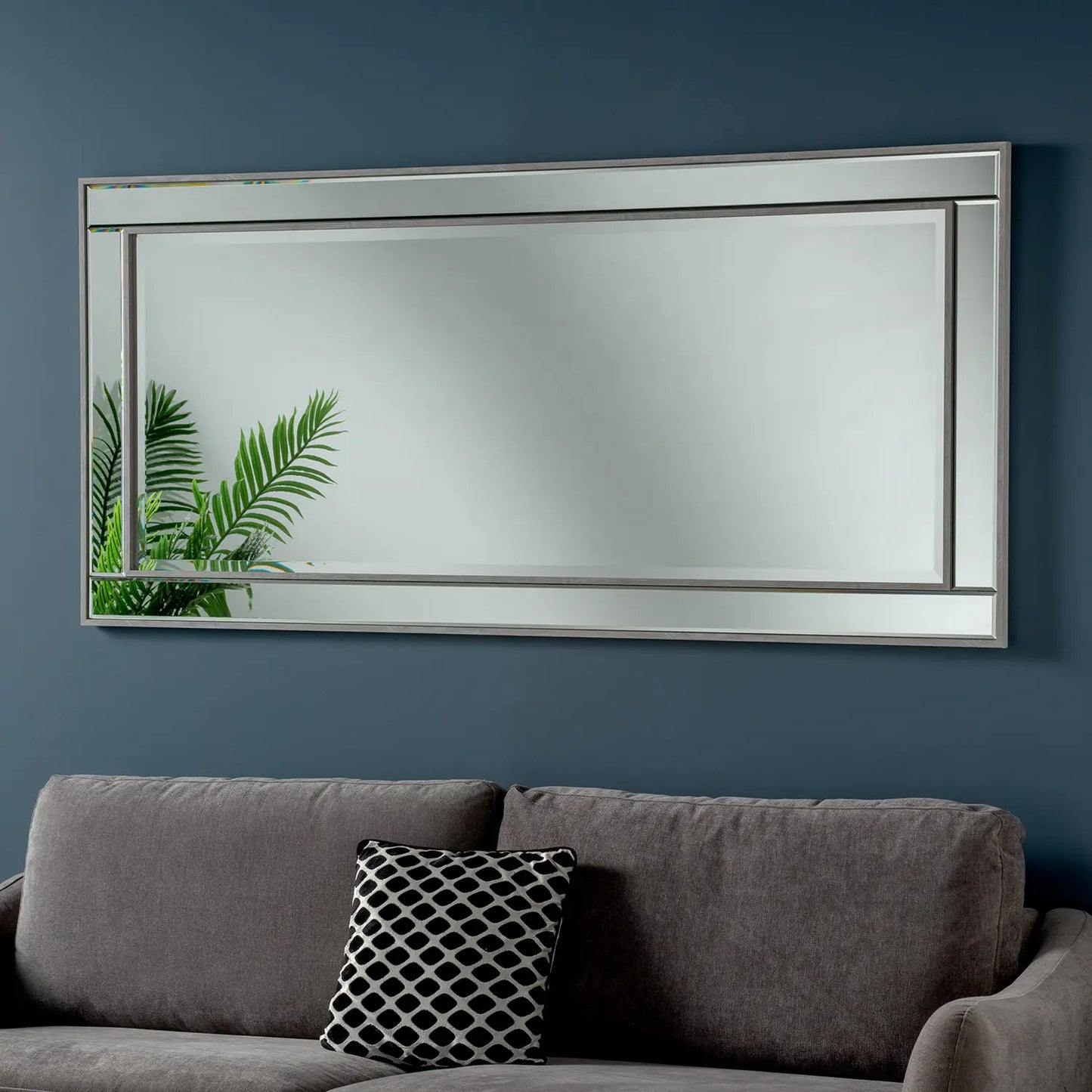 Extra-Large, framed grey beveled mirror, mounted on a dark blue wall, next to a grey couch.