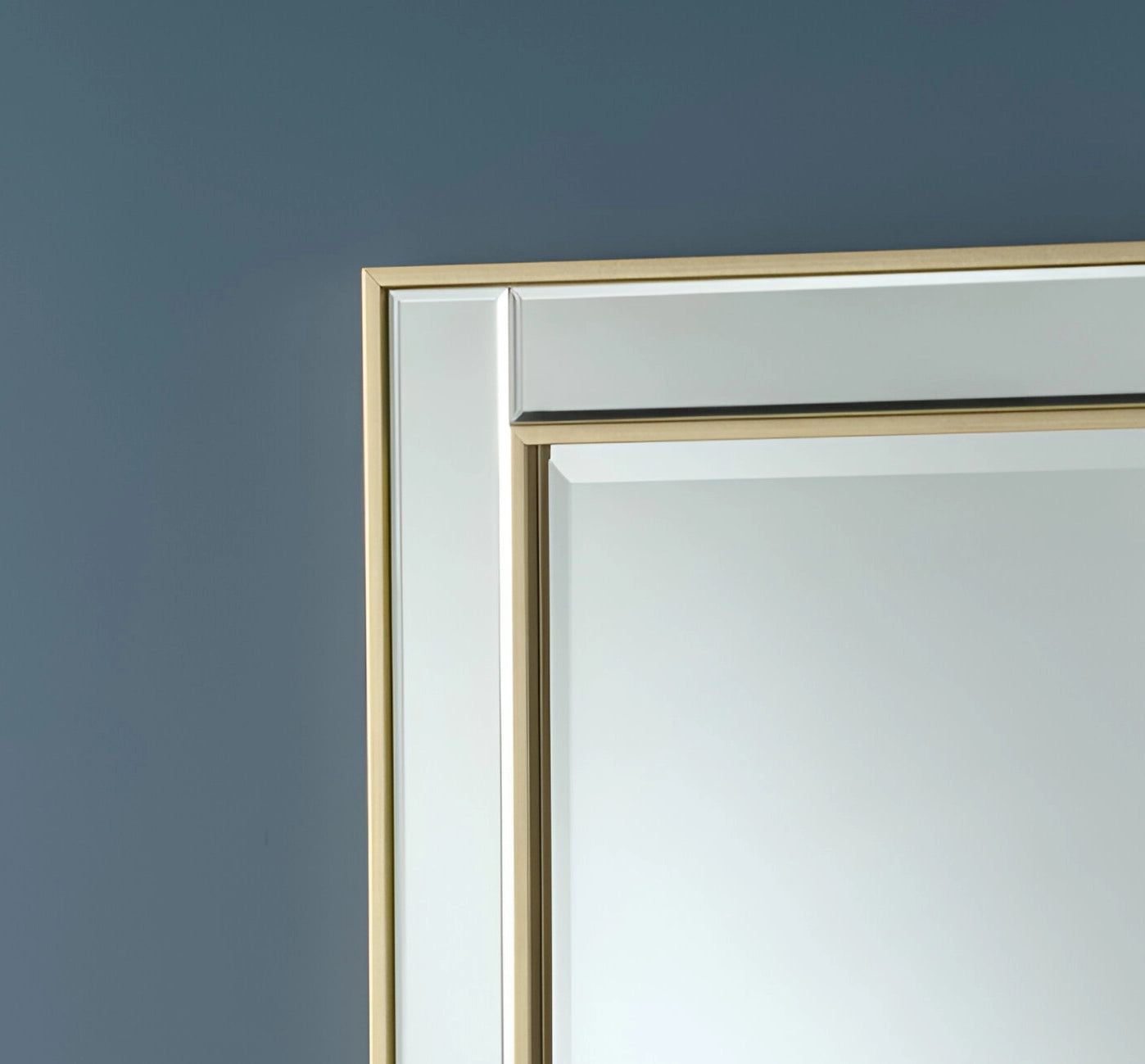 Gold-framed rectangular mirror corner. Detail of the double frame and beveled finish.