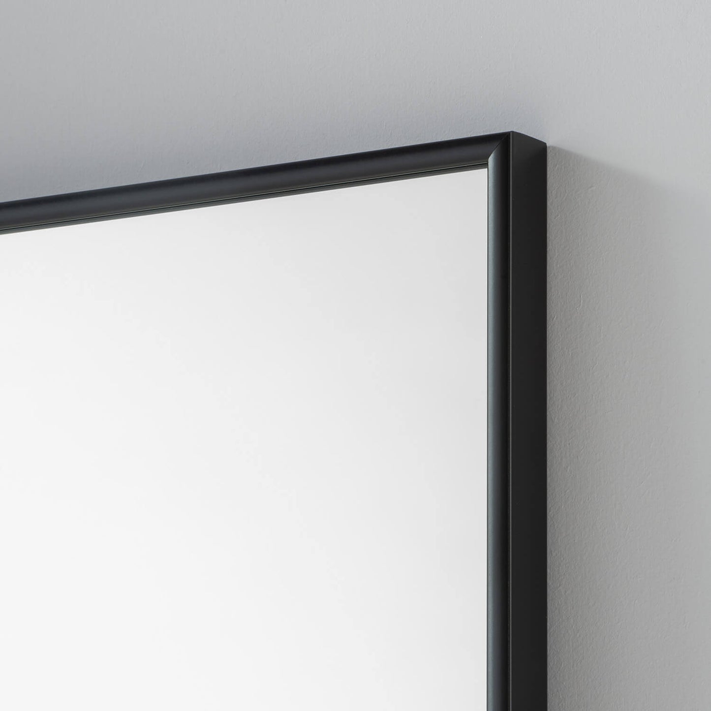 Black framed rectangular mirror against a light grey wall. Close-up of the frame.