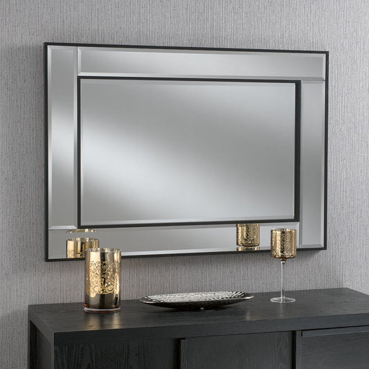 Large rectangular framed mirror with black borders, displayed on a dark wooden console table with decorative gold candle holders and a decorative plate.