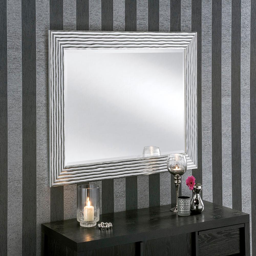 Large silver framed mirror with textured frame, placed on a dark wooden console table against striped wallpaper.