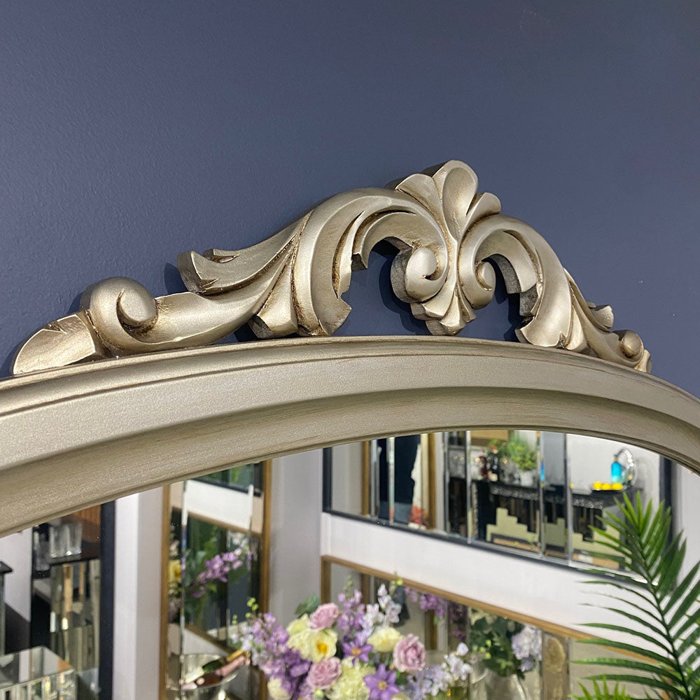 Ornate, arched, silver-toned mirror with decorative carvings.
