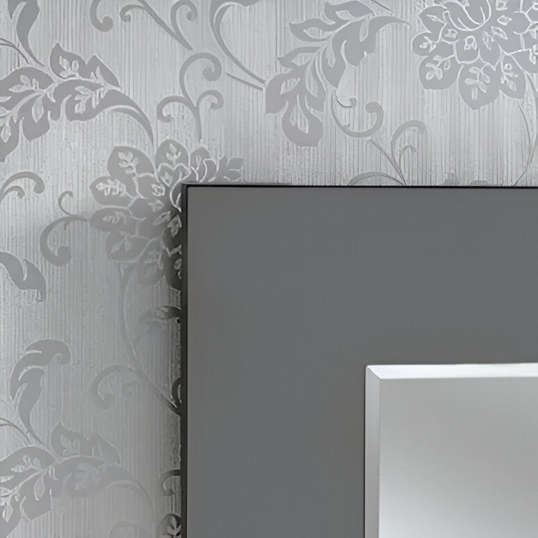 Corner of a dark grey framed mirror against a wall with a light grey floral wallpaper.